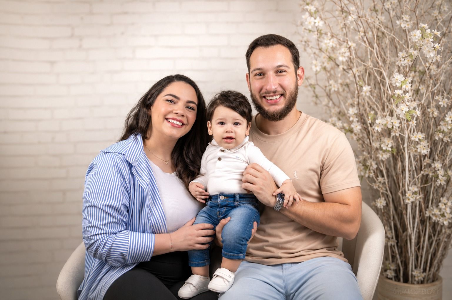 Pai, mãe e bebê sentados juntos no estúdio, em frente a um arranjo de flores secas